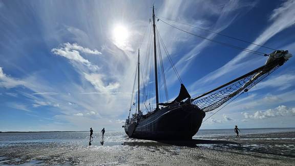 The tjalk Aagtje resting on the tidal flats with people beside the ship