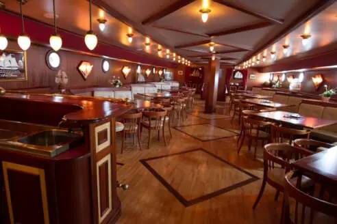 Wood-panelled saloon with a bar and tables aboard the Abel Tasman