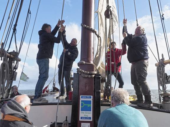 Guests hoisting a sail together on the deck of the Boekanier