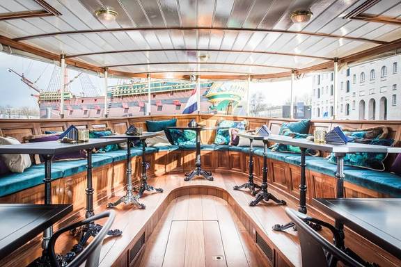 Bright saloon of the Dame van Amstel with wooden tables and turquoise benches