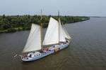 Aerial view of De Hester sailing beside a green riverbank