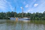 De Hester with sails lowered beside a green riverbank