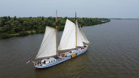 Aerial view of De Hester sailing beside a green riverbank