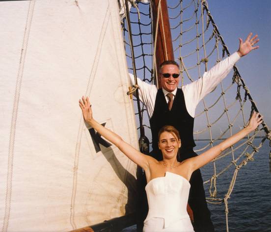 Wedding couple posing with outstretched arms beside the sails of the Frisius van Adel