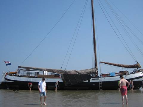 Tjalk Nieuwe Zorg resting on the tidal flats with guests beside the ship