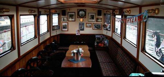 Wood-panelled saloon with benches and tables aboard the Oude Maze