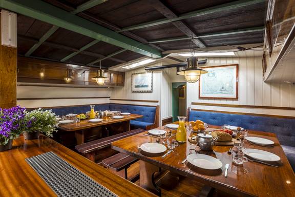 Wood-panelled saloon of the Spes Mea with set tables and blue benches