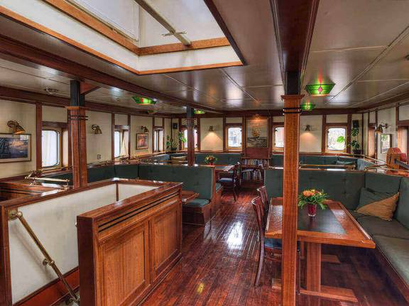Wood-panelled saloon of the Thalassa with tables and green benches