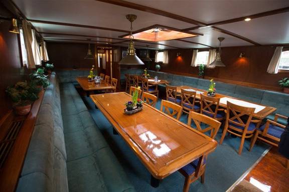 Saloon with wooden dining tables and green benches aboard a sailing ship
