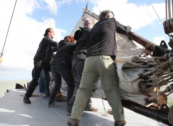 Guests on deck beside the wheel of a sailing ship