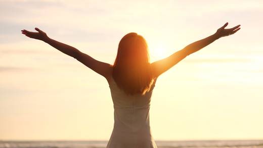 Woman with outstretched arms beside the water at sunset