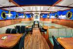 Dining room with wooden tables and portholes on the Mare fan Fryslân
