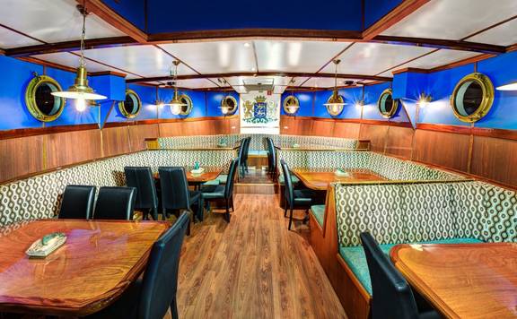 Dining room with wooden tables and portholes on the Mare fan Fryslân