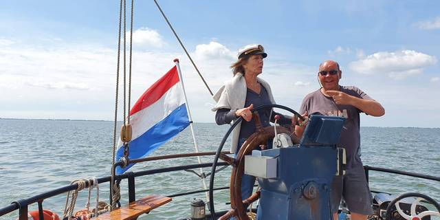 Two guests at the wheel of a sailing ship